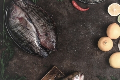 top view of raw fish, chili peppers, shrimp, herbs with lemons and tablecloth on dark table top